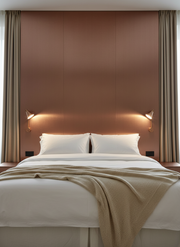 Modern bedroom with a bed, headboard lights, and beige walls.