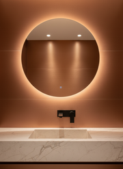 Round illuminated mirror on a wall with a sink below in a bathroom setting.